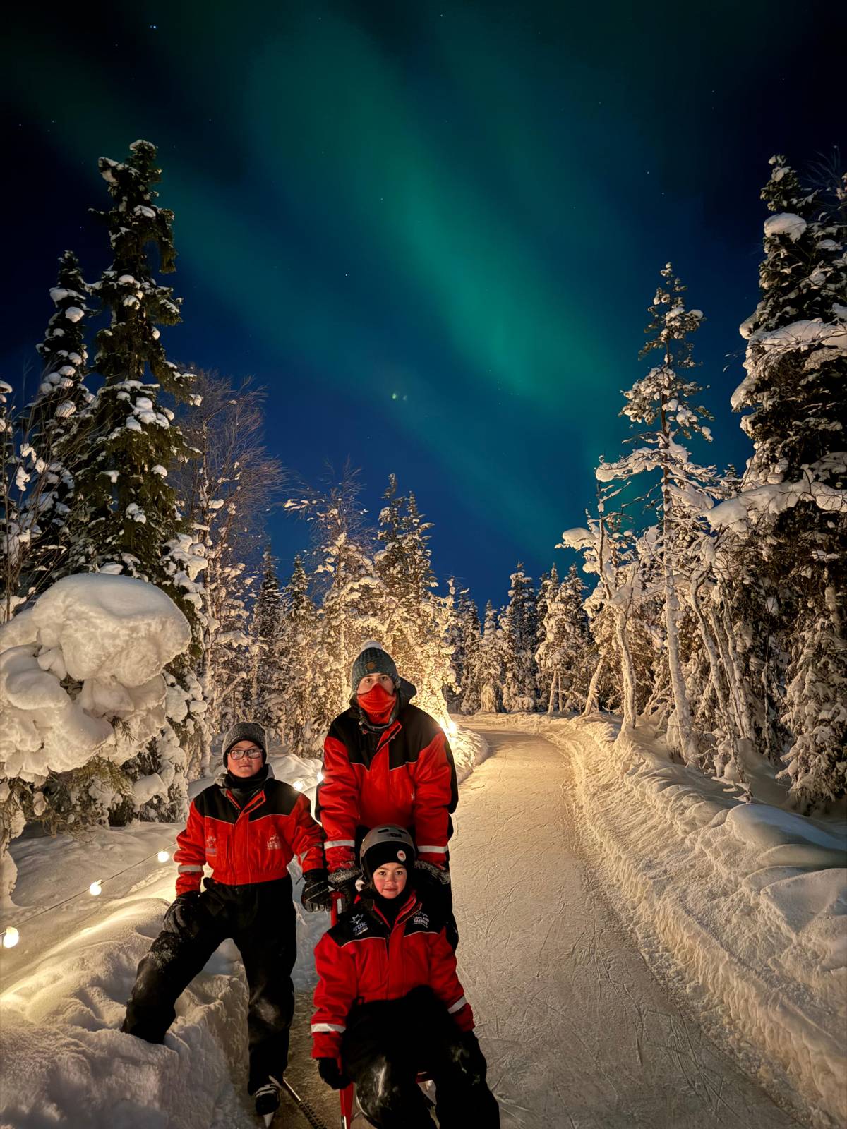 A family with a kicksled on the trail under the aurora