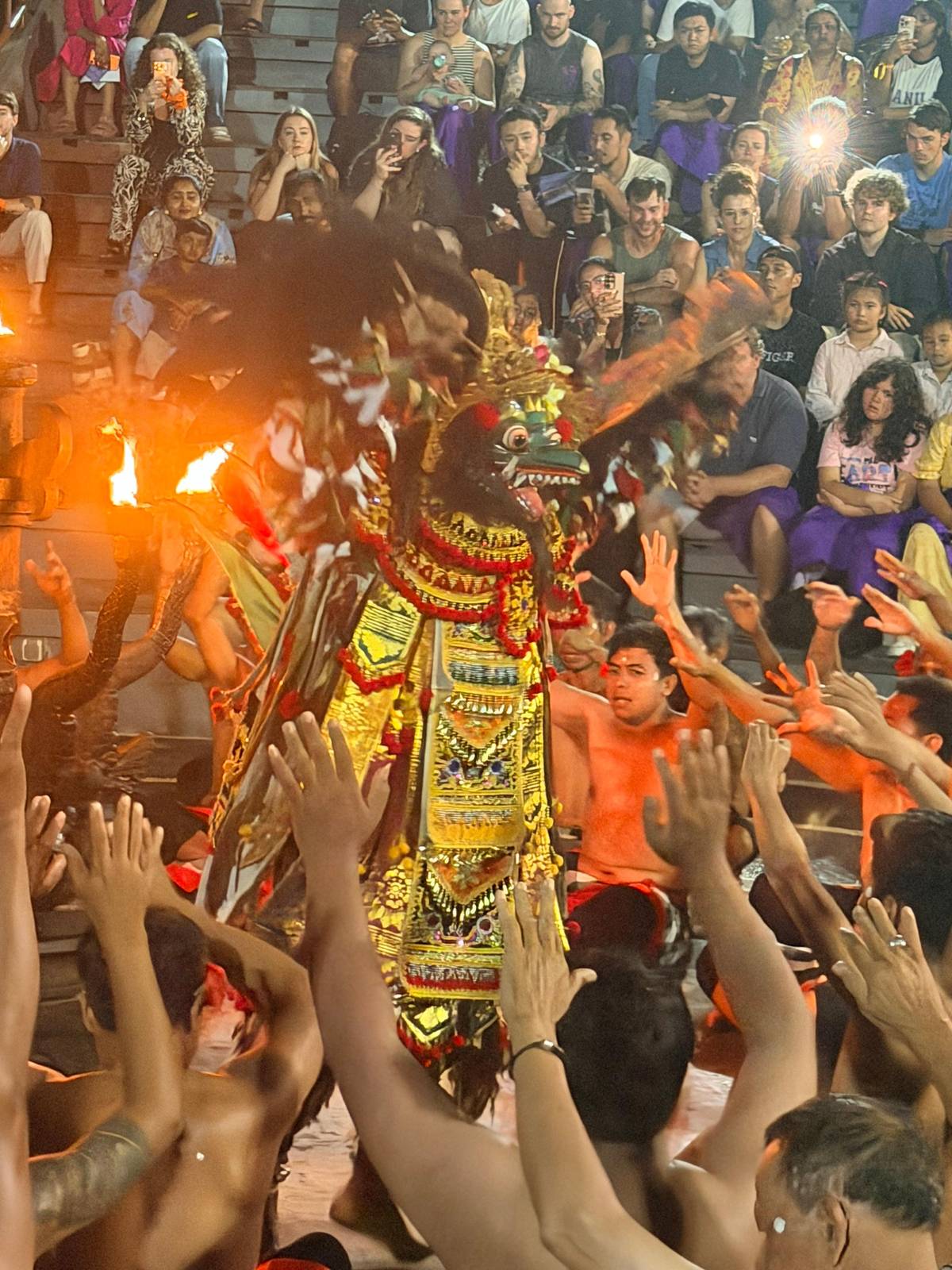 Torches and raised hands around a masked dancer