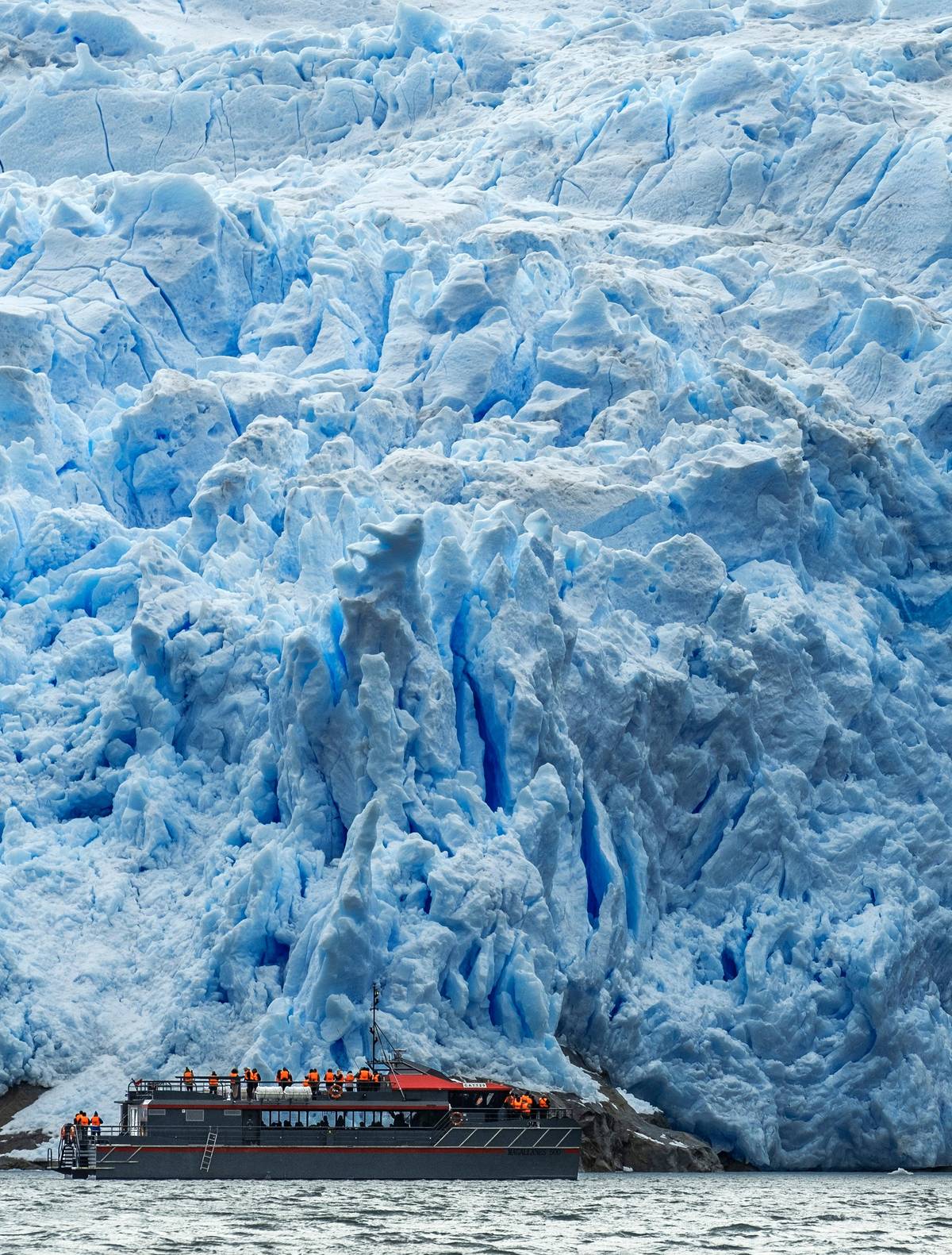 The boat dwarfed by a blue glacier front
