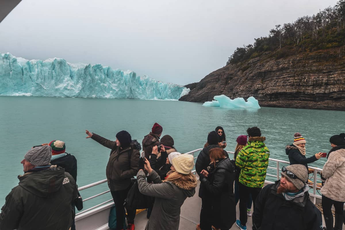 Guests on a boat deck facing the glacier