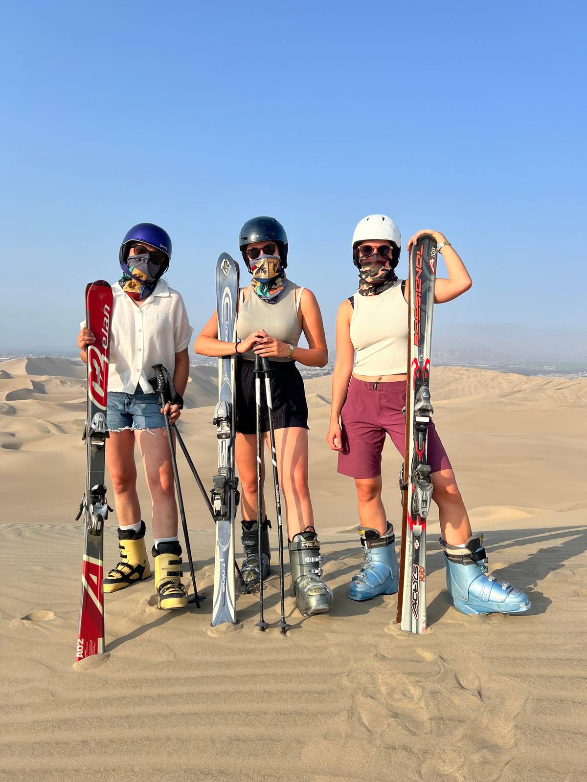 Three riders holding skis and poles on a dune top