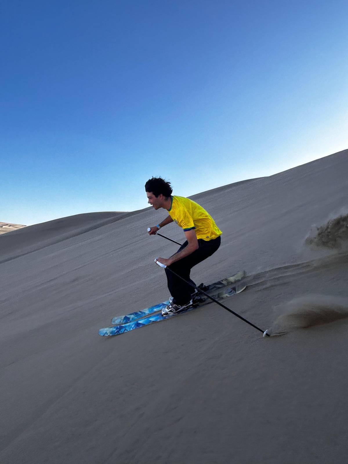 A skier spraying sand on a dune under a blue sky