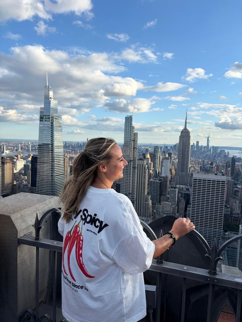 A visitor leaning on the open-air 70th-floor rail with nothing at eye level, One World Trade Center standing downtown behind them