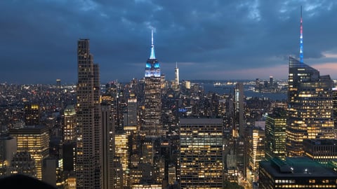 Night over Midtown with the Empire State Building lit blue above the grid of lit office floors