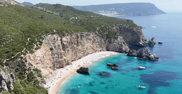 Small pebble cove with turquoise water at the foot of tall cliffs, seen from the sea