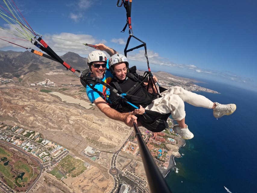 Tandem paraglider soaring above a rocky coastline and the sea
