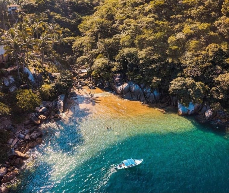 Aerial view of a small golden cove hemmed in by boulders and dense jungle, with one open panga anchored in turquoise water