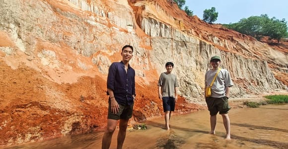 Three people standing ankle-deep in a shallow stream between orange and white layered sandstone walls