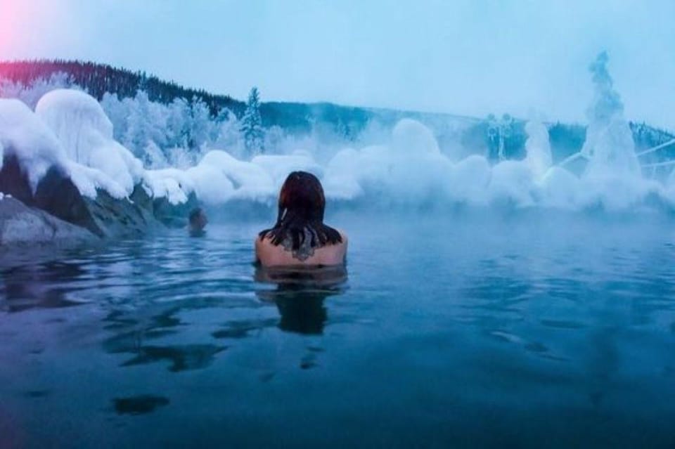 Steam rising from an outdoor hot-spring pool surrounded by snowy spruce trees