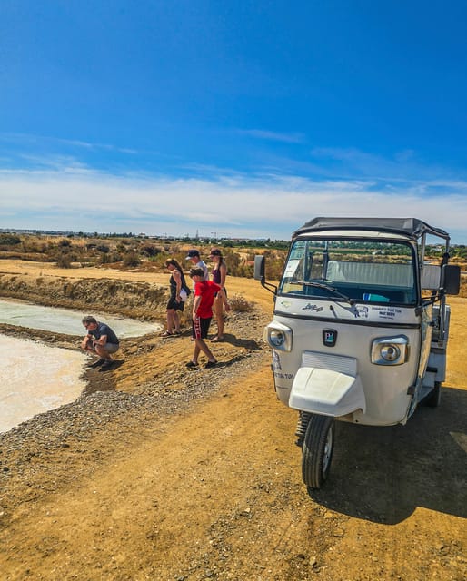Ein weißes Tuk-Tuk steht auf einem Sandweg neben einem Salzbecken, davor eine kleine Gruppe