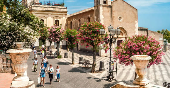 Taormina’s hillside buildings above the blue Ionian coast with Mount Etna in the distance