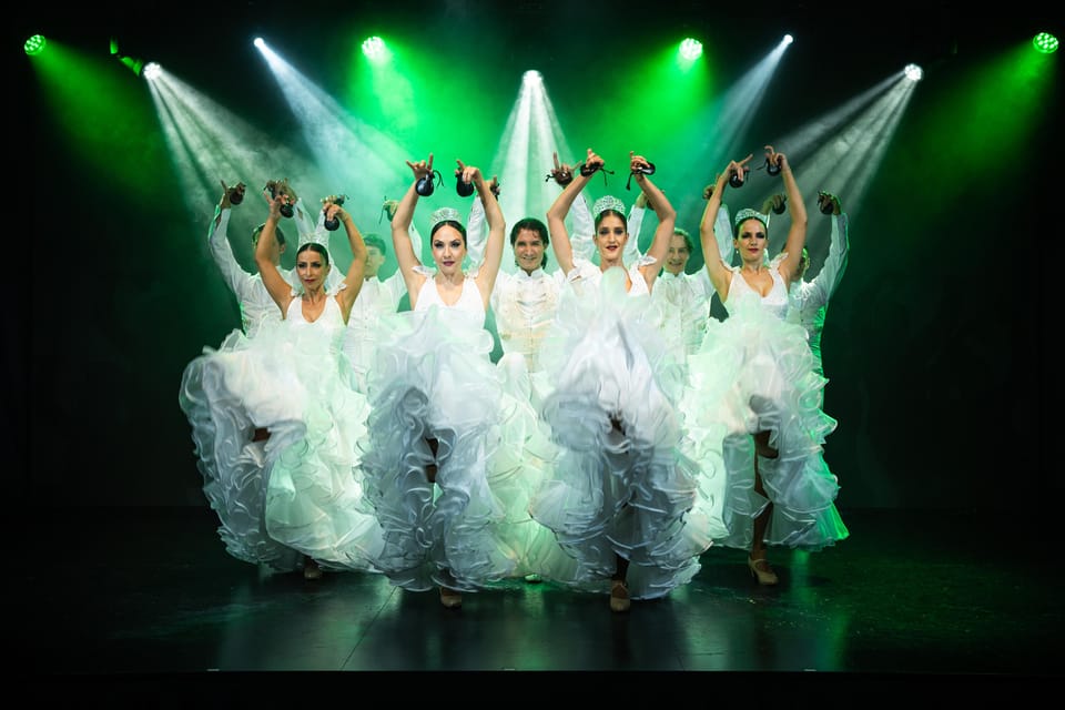 Flamenco dancers in white ruffled dresses raising castanets under green stage spotlights