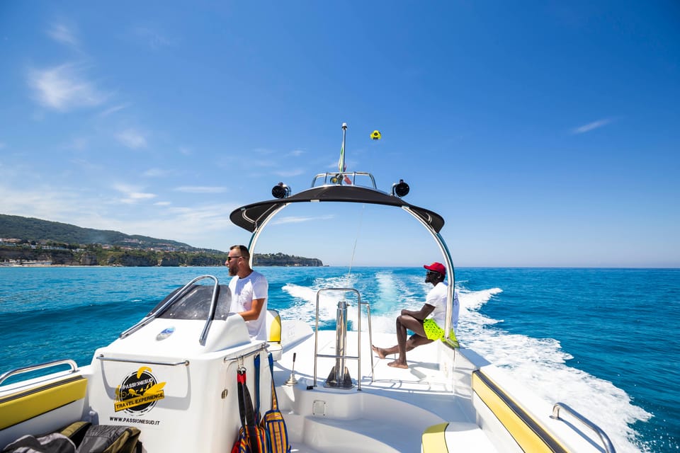 A parasail canopy carrying a pair of passengers above the blue sea off Tropea