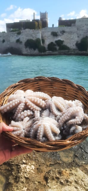 A hand holding a wicker basket of small octopus above the water, with a stone fortification wall behind