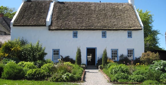 A whitewashed thatched cottage beside a grassy lane