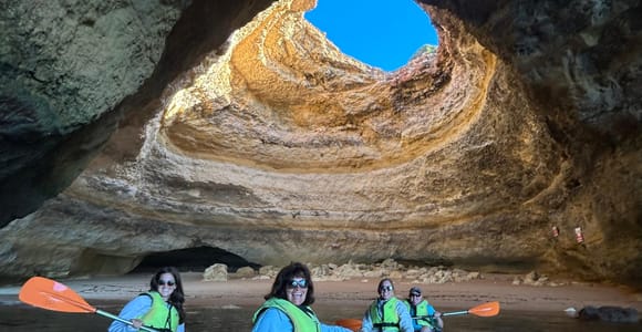 Paddlers in life jackets in two blue kayaks inside a sea cave, with a round opening in the roof above