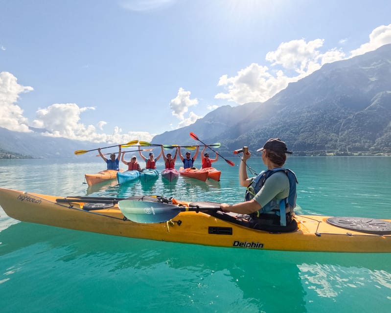 A group of kayakers raising their paddles on bright turquoise water, with a kayak guide photographing them