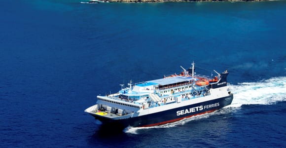 White and dark blue passenger ferry crossing deep blue open sea with a white wake