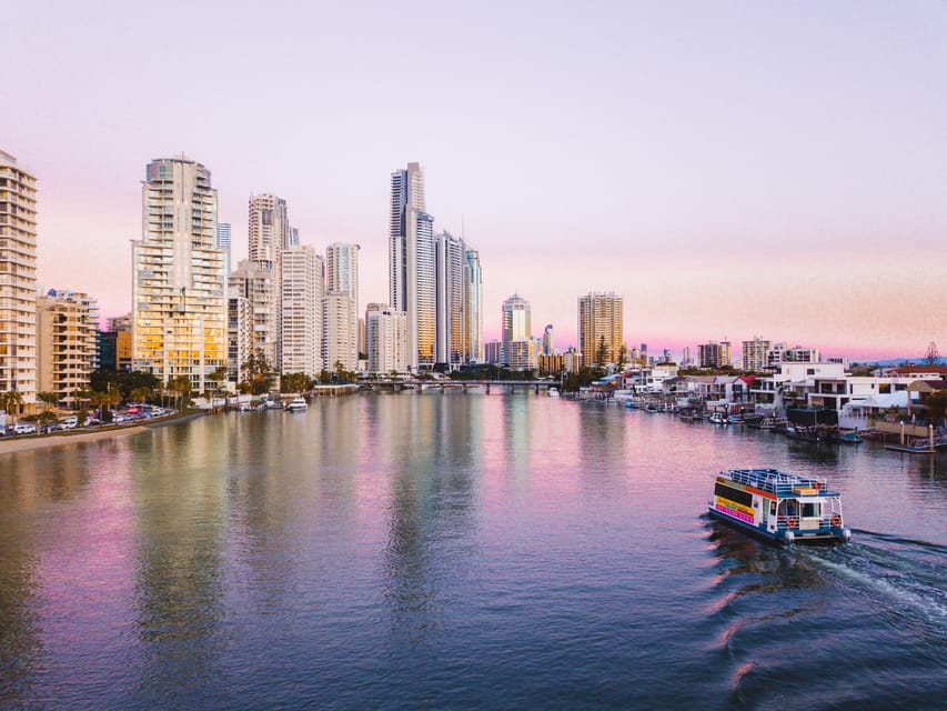 A sightseeing boat passing waterfront homes on the Nerang River beneath the Surfers Paradise skyline