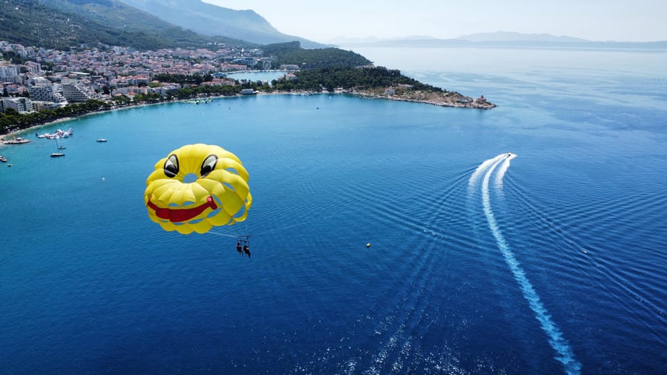 A parasail canopy above a bay with moored boats and a mountain behind