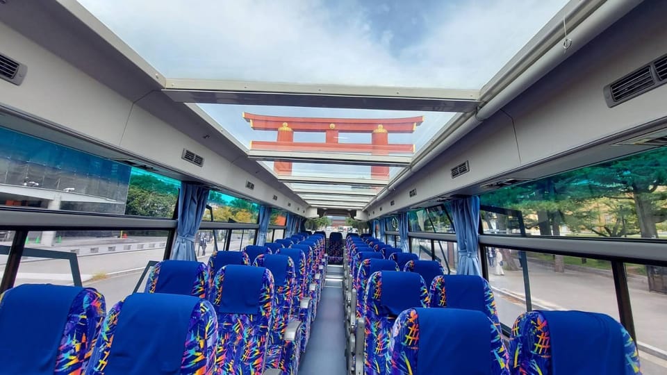 The inside of an open-top sightseeing coach with blue patterned seats, a large vermilion torii framed in the roof opening ahead