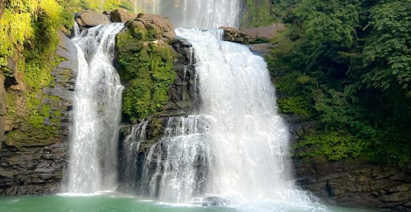 Two tiers of Nauyaca Waterfalls falling into a green jungle pool