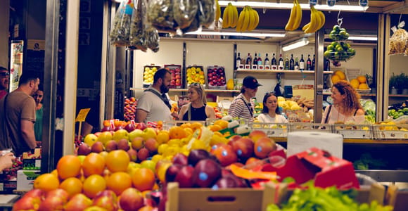Fruit and vegetable stalls in a market hall in Bologna, with visitors and vendors in front