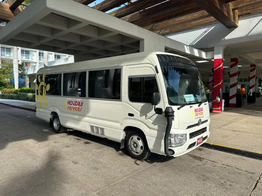 A white minibus marked Holiday Services parked under a covered hotel driveway in bright sunlight