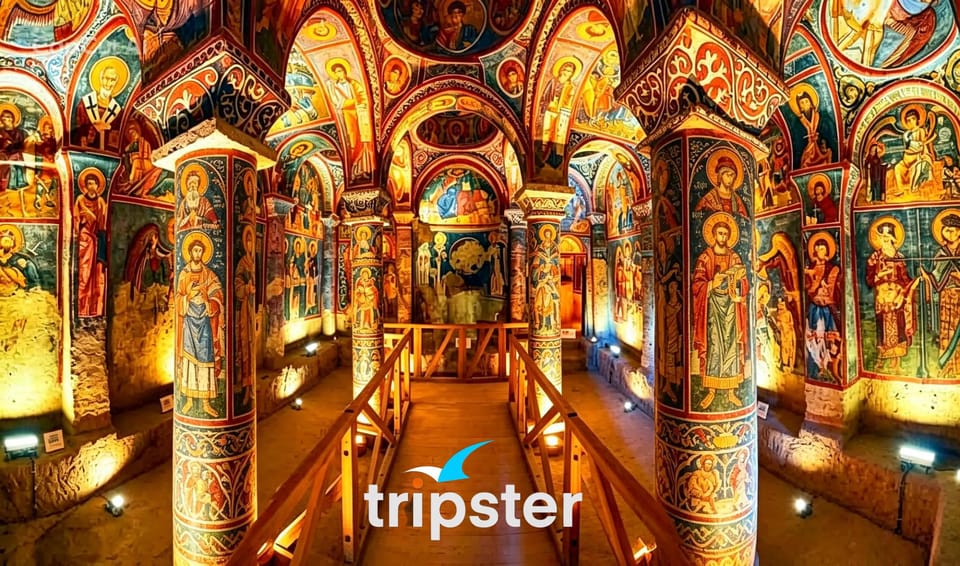 Interior of a rock-cut church with painted columns and walls covered in frescoes, a wooden walkway in the middle