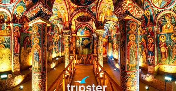 Interior of a rock-cut church with painted columns and walls covered in frescoes, a wooden walkway in the middle