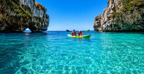 Two people paddling a green tandem kayak on turquoise water between two limestone cliffs