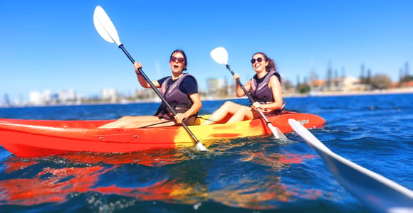 Orange kayaks pulled onto a sandy Wave Break Island beach beside clear Broadwater shallows