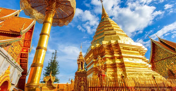 The gilded chedi of Doi Suthep under a pierced golden umbrella, red temple roofs on either side against a deep blue sky