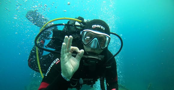 Diver above dark volcanic rock in clear blue water