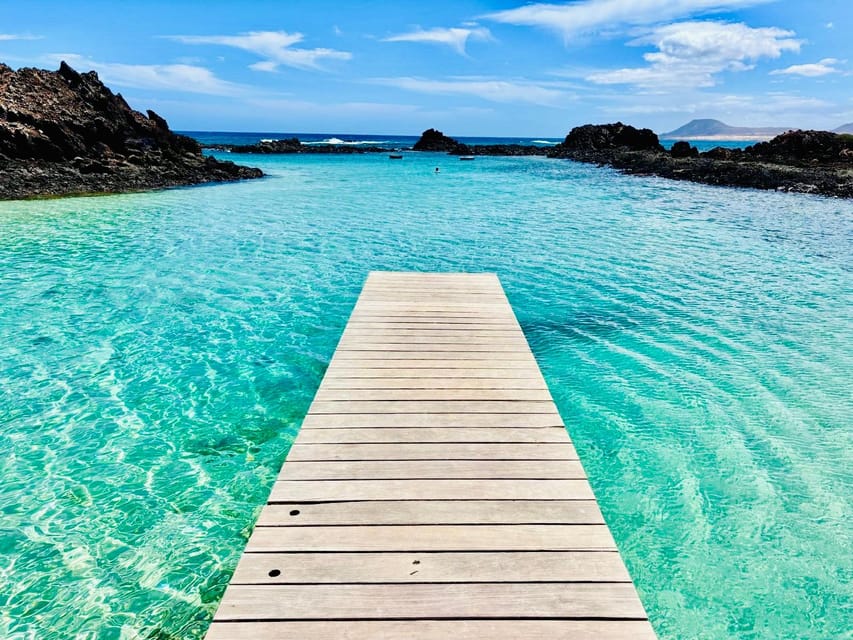 A narrow road crossing pale dunes towards turquoise water