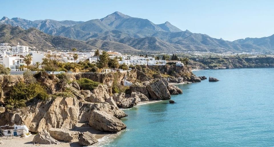 White houses above rocks and turquoise sea with mountains behind