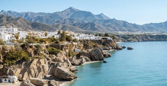 White houses above rocks and turquoise sea with mountains behind