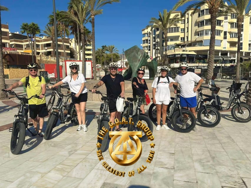 A group in helmets stands beside e-bikes on a palm-lined promenade