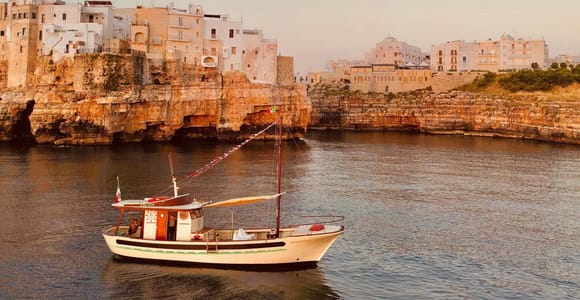 A traditional wooden boat moving along the limestone coast in warm evening light