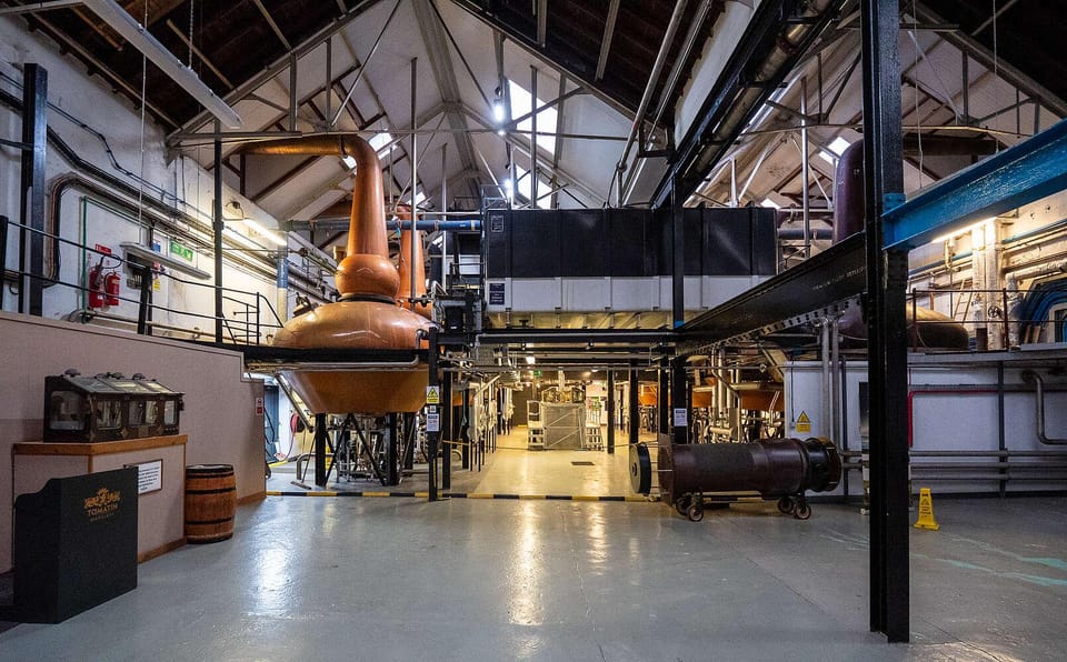 Copper whisky stills and curved pipes inside a warm-lit Scottish distillery