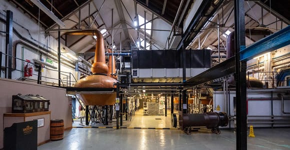 Copper whisky stills and curved pipes inside a warm-lit Scottish distillery
