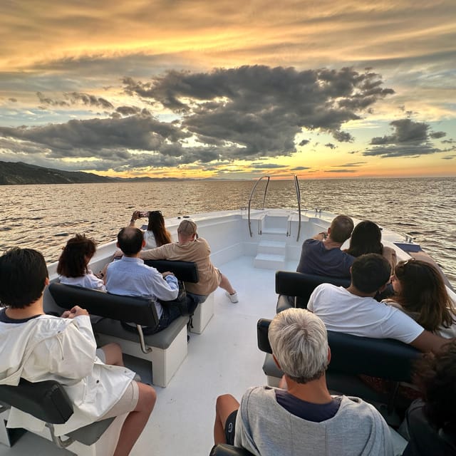 Passengers on the white deck of a boat watching an orange sunset sky over the sea