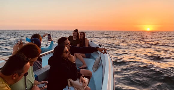 People on a small boat watching the sun set over the open sea