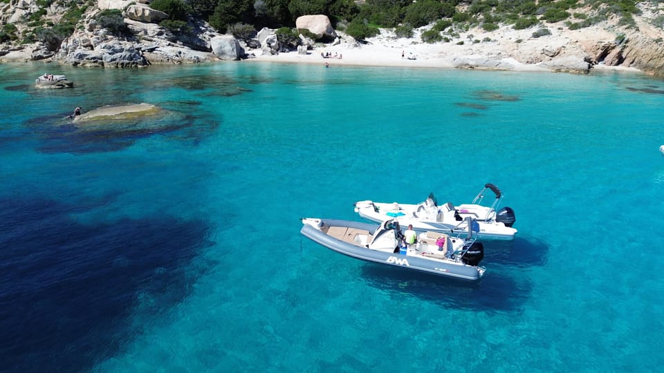 Two small boats at anchor in turquoise water off a white-sand cove with granite rocks