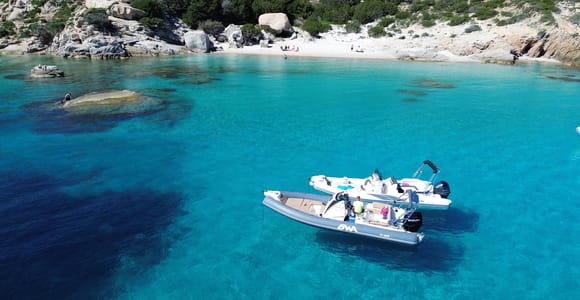 Two small boats at anchor in turquoise water off a white-sand cove with granite rocks