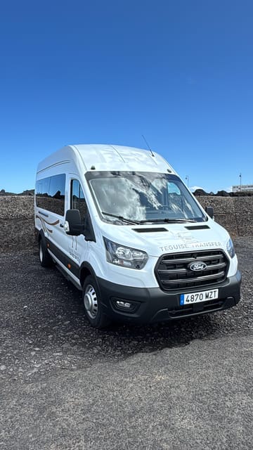 A white transfer minibus parked on dark gravel under a blue sky