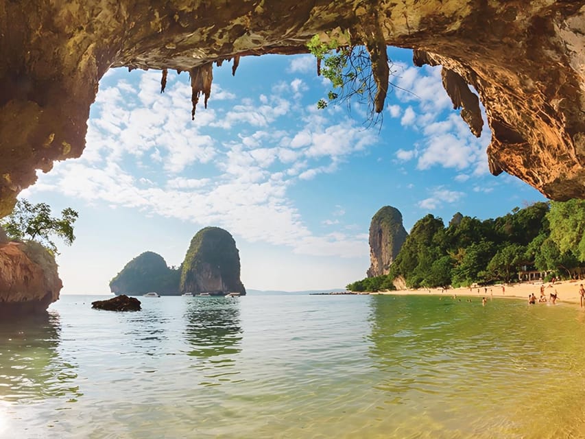 Longtail boats moored off a sandy beach beneath an overhanging limestone headland at golden hour