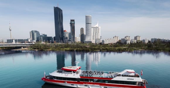 Red and white passenger ship on the Danube with the high-rise skyline of the Donau City district behind it