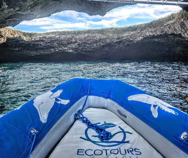 View from the bow of an inflatable boat with a humpback whale painted on its tube, looking out of a rock arch towards grass-topped cliffs
