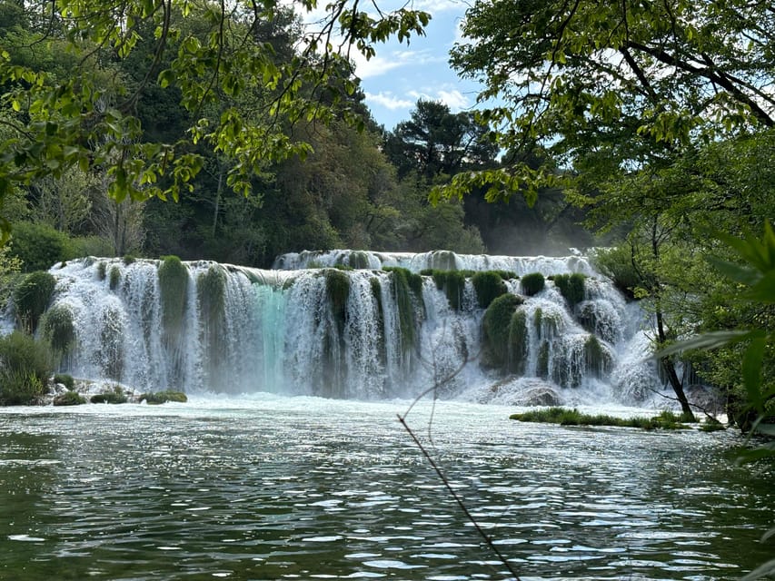 Wide curtain of waterfalls spilling over mossy travertine steps into a green pool